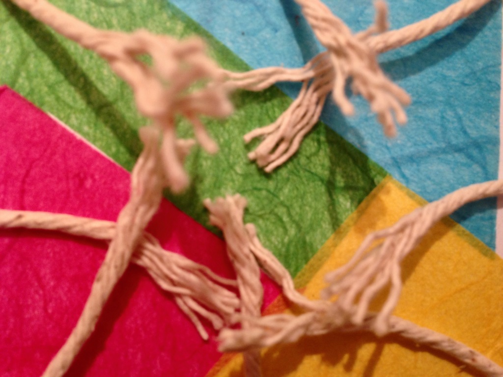 Frayed pieces of string on top of colourful scraps of paper.
